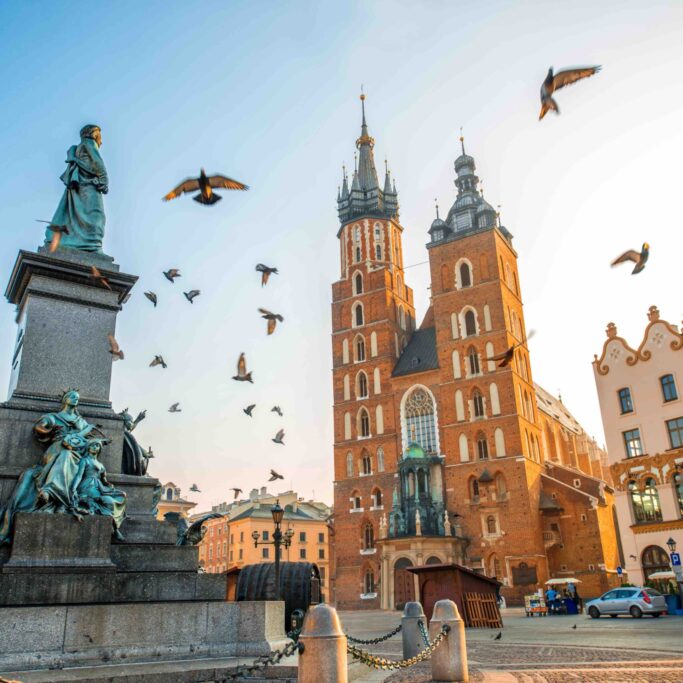 Old city center view with Adam Mickiewicz monument, St. Mary's Basilica and birds flying in Krakow on the morning